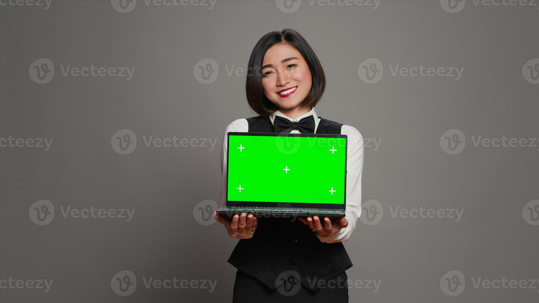 Receptionist showing greenscreen display on personal laptop, presenting isolated copyspace mockup on screen. Asian hotel employee holding pc with chromakey mockup template. Camera A. photo