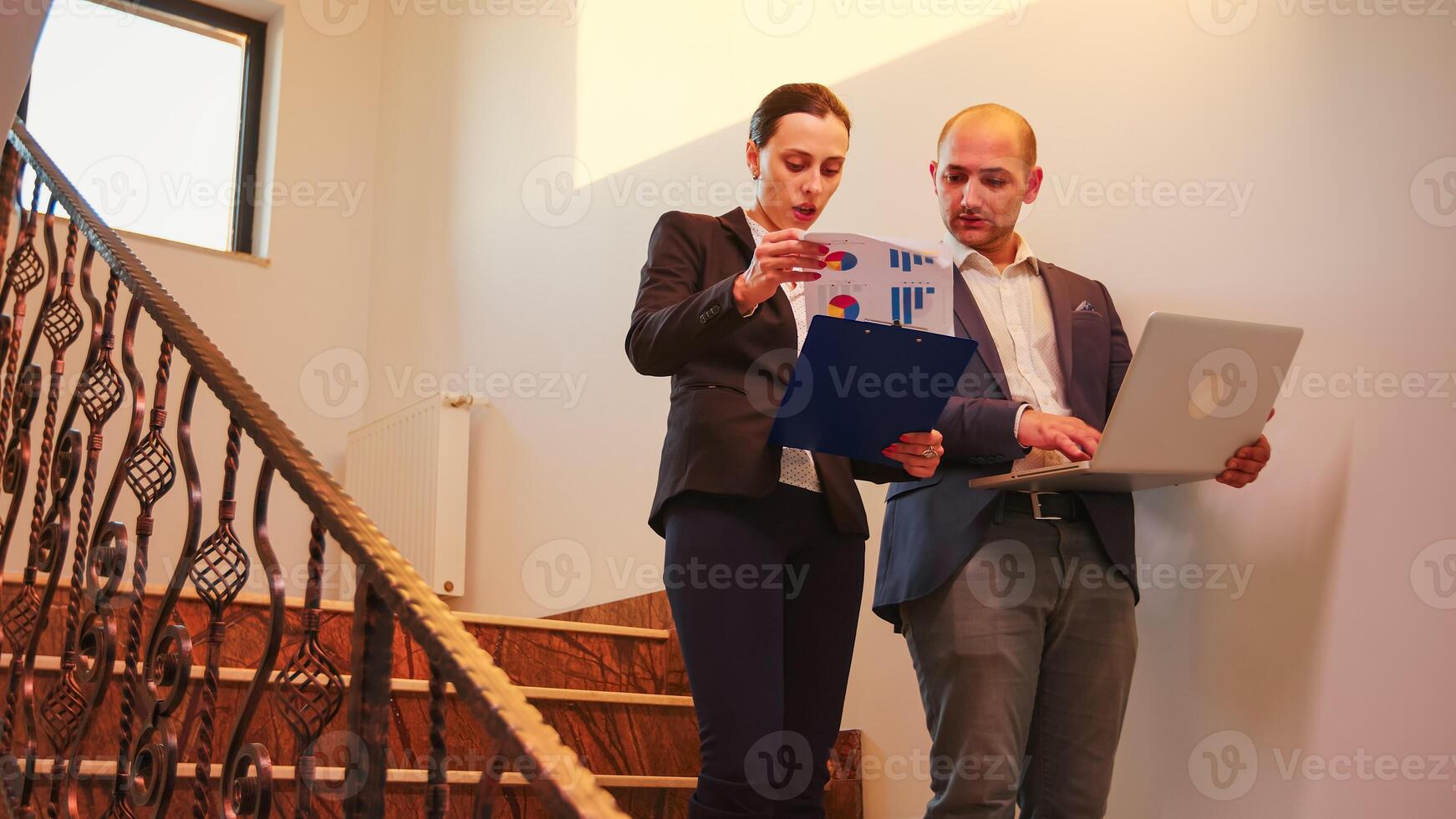 Businesswoman talking with corporate executive manager on staircase of business building looking on laptop. Professional successful entrepreneur in team working overtime in modern office stairs. photo