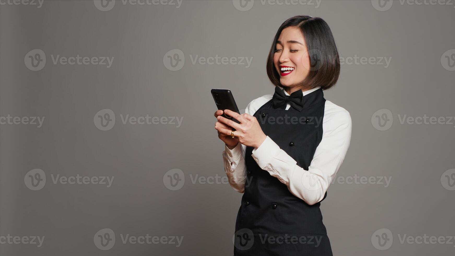 Restaurant hostess texting messages to confirm reservations on phone app, working in catering and serving industry. Asian waitress using smartphone online websites, social media. Camera A. photo