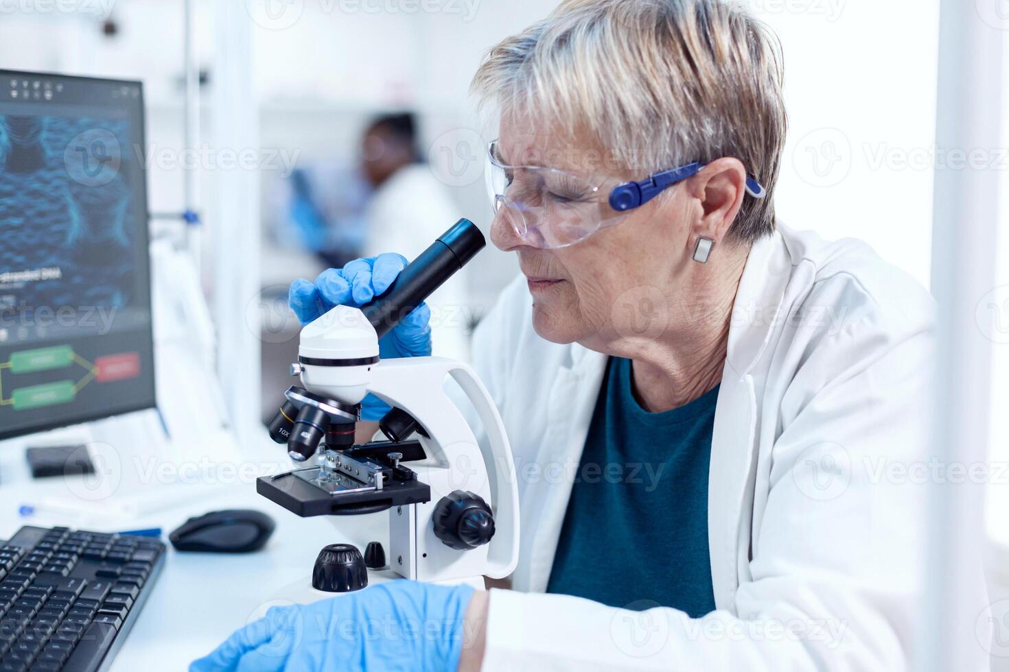 Close up of senior scientist in medical industry working in laboratory using microscope. Elderly researcher carrying out scientific research in a sterile lab using a modern technology. photo