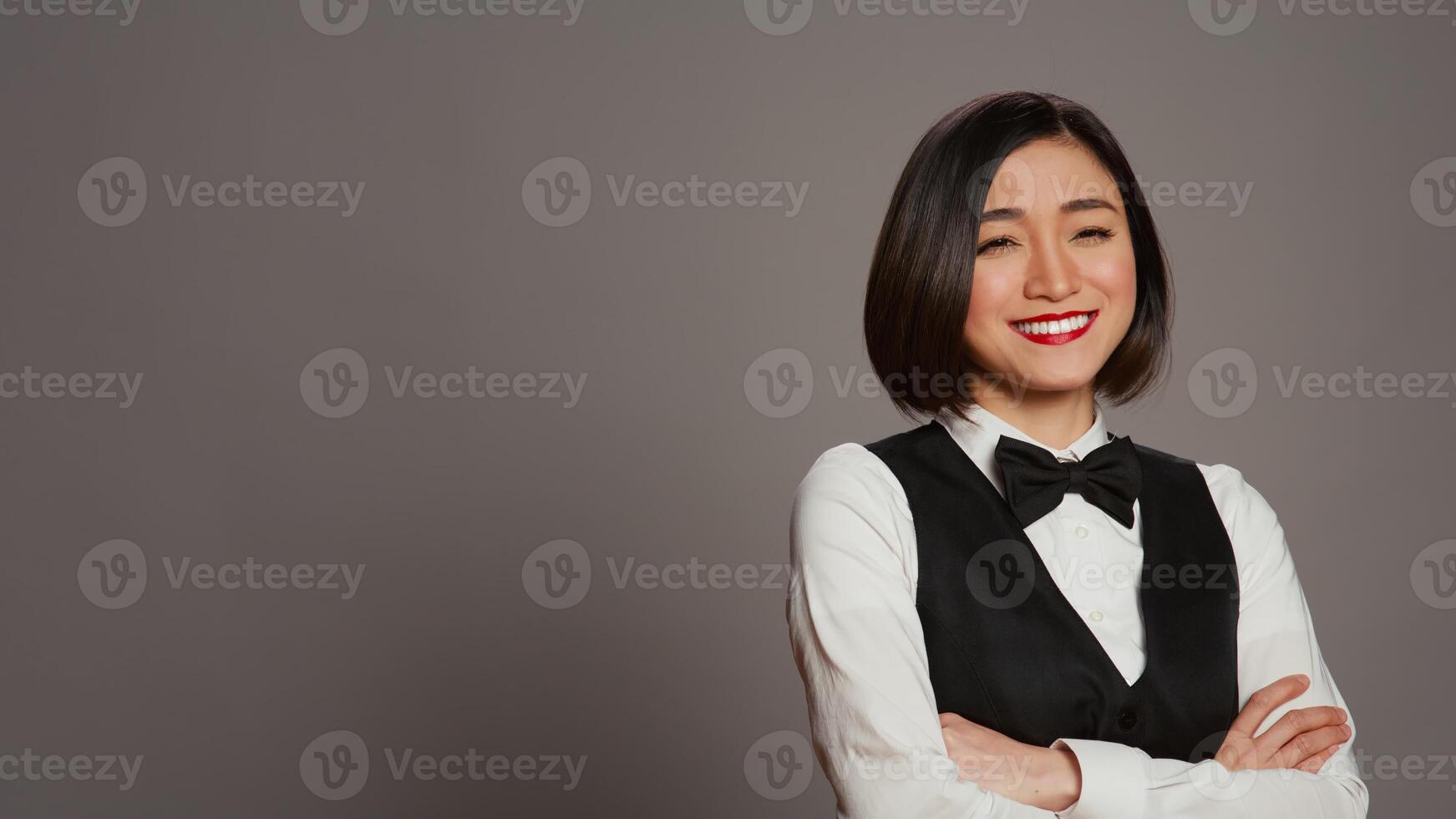 asiático recepcionista posando con brazos cruzado en cámara, sensación confidente y profesional en un formal traje y atar. mujer con frente escritorio personal ocupación, saludo invitados en estudio. cámara b. foto