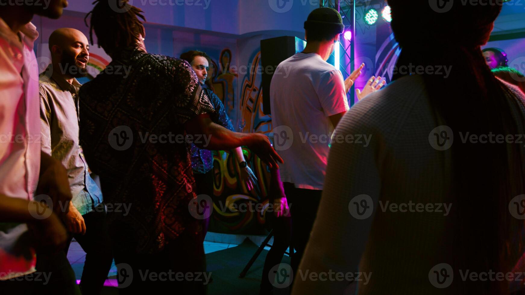 Diverse people partying at nightclub, enjoying disco party on dance floor with cool DJ music. Smiling men and women having fun together at discotheque, celebration event. Handheld shot. photo