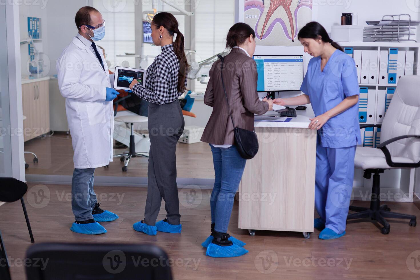 Orthodontist using tablet explaining dental x ray to patient standing in waiting area of stomatologic office. Dentist showing to woman radiography using digital device working in modern clinic. photo