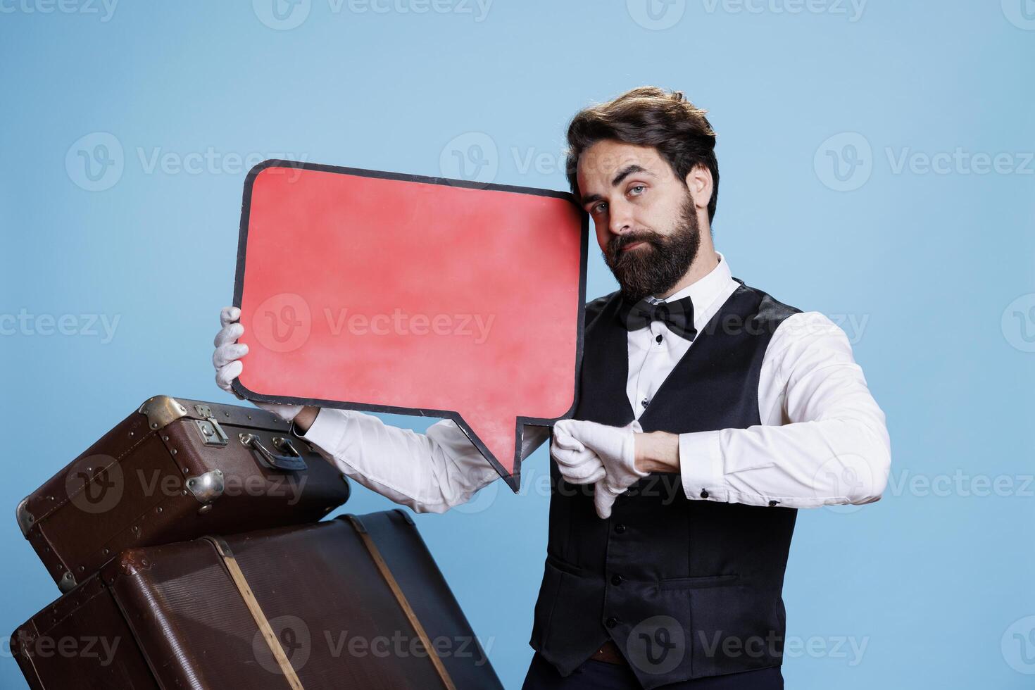 profesional portero usos habla burbuja rojo firmar en estudio mientras él lo hace pulgares abajo negativo símbolo. botones presentación anuncio con aislado blanco copyspace cartelera, sensación insatisfecho. foto