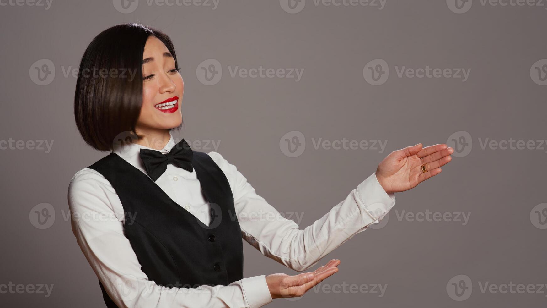 Reception staff doing web advertisement over grey background, pointing at something aside for a marketing commercial. Asian employee working on a promotional ad in studio. Camera B. photo
