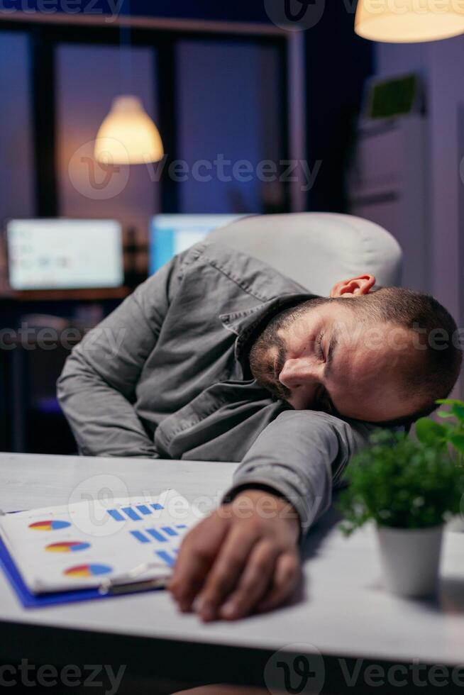 Manager napping on desk because of overwork in workplace. Workaholic employee falling asleep because of while working late at night alone in the office for important company project. photo