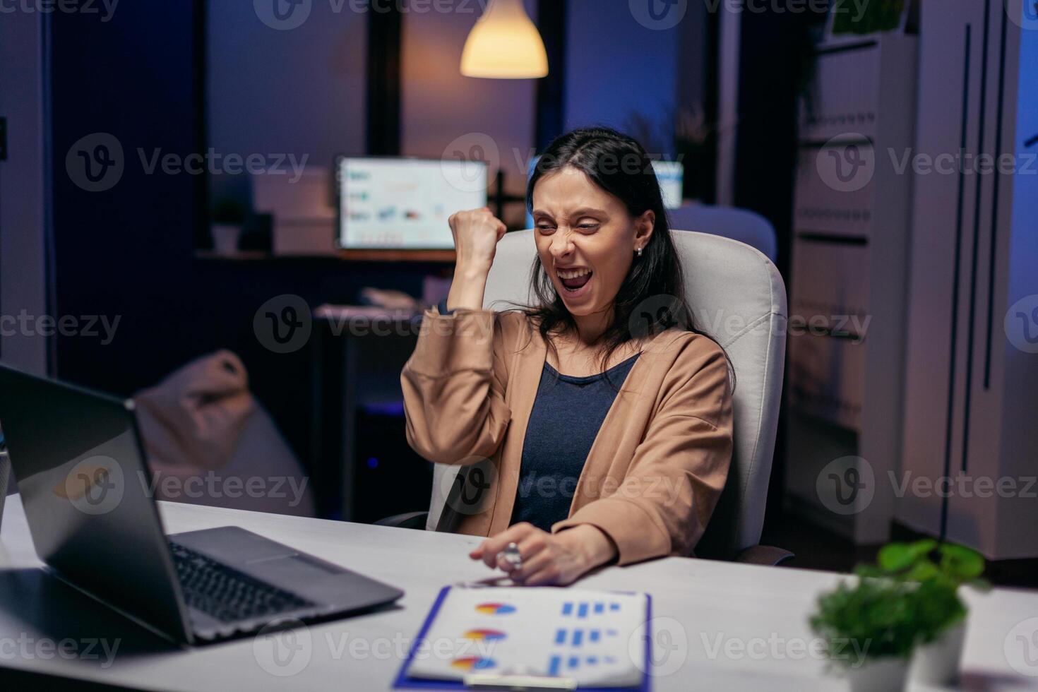 Cheerful ntrepreneur, feel ecstatic reading great online news on laptop working overtime. Excited woman working late night hourse in the office because of successful project. photo