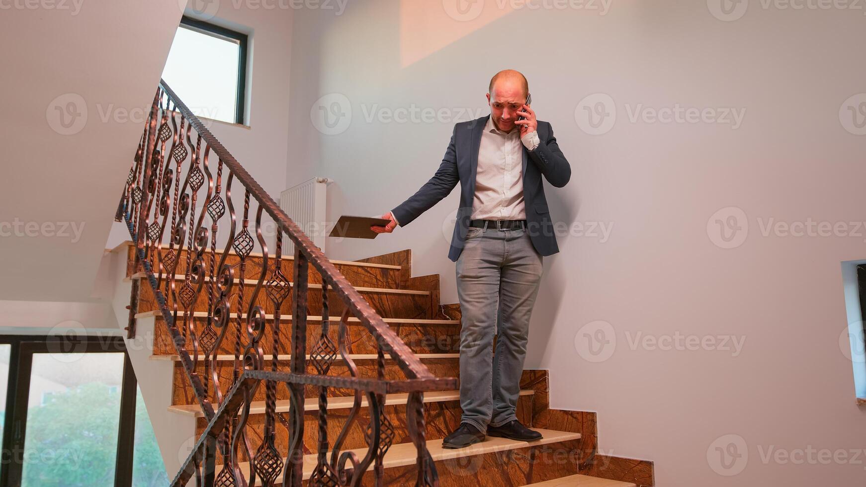 Nervous office executive speaking on smartphone standing on stairs in finance corporate company working overtime. Group of professional successful businesspeople working in modern finacial building. photo
