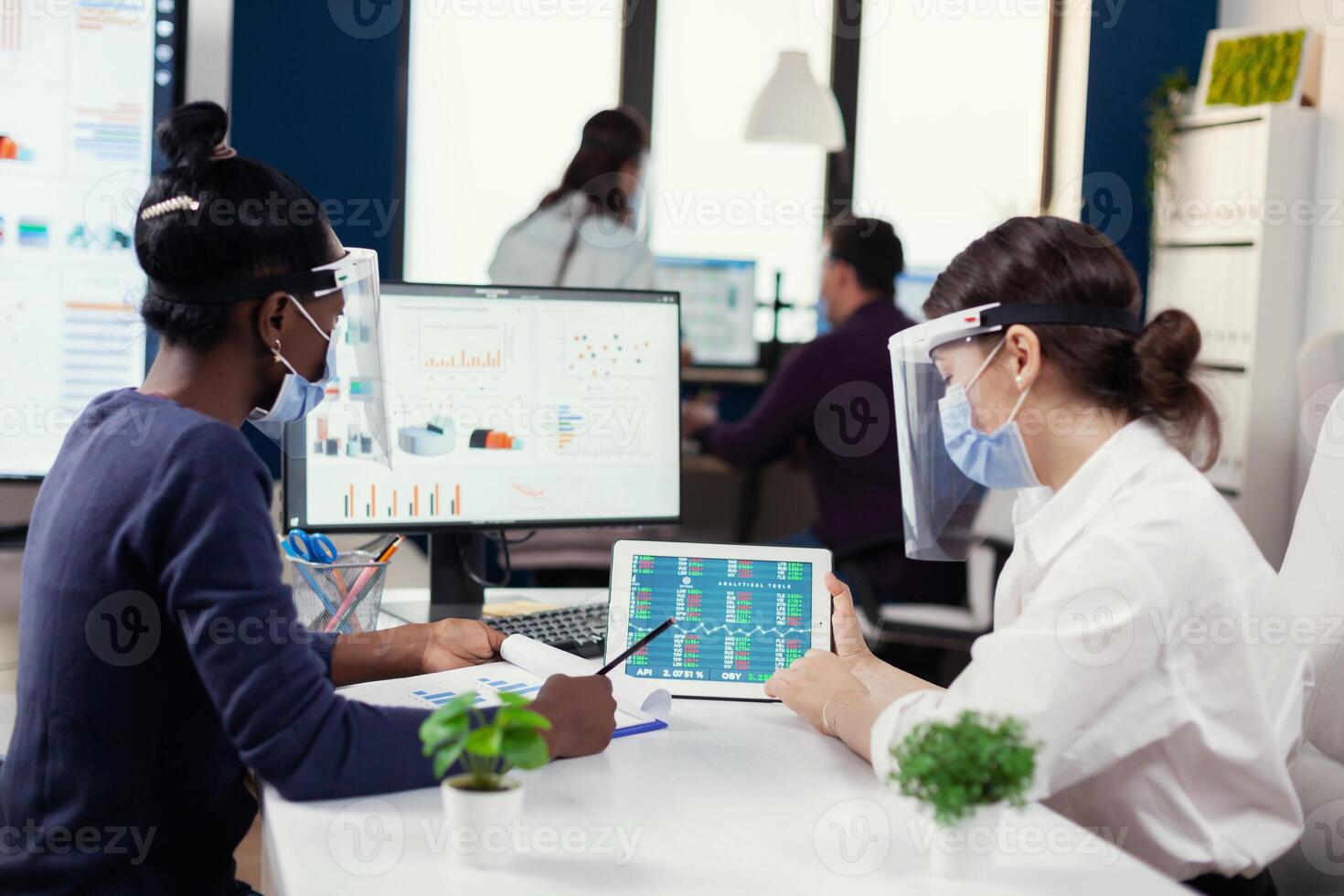 financiero equipo de grande sociedad haciendo financiero análisis vistiendo cara máscara durante COVID-19. diverso grupo de negocio personas trabajando y comunicado juntos en oficina con nuevo normal, respecto a social distancia. foto