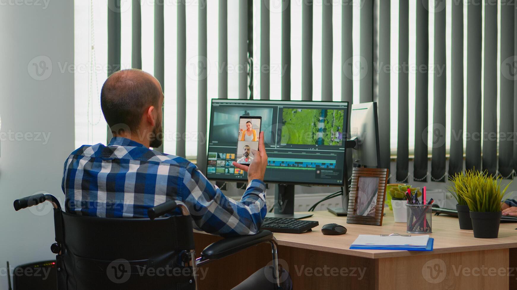 Handicapped videographer in wheelchair talking on webcam with cowerkers while editing a video project creating content in modern company office. Creator blogger working from photo studio.