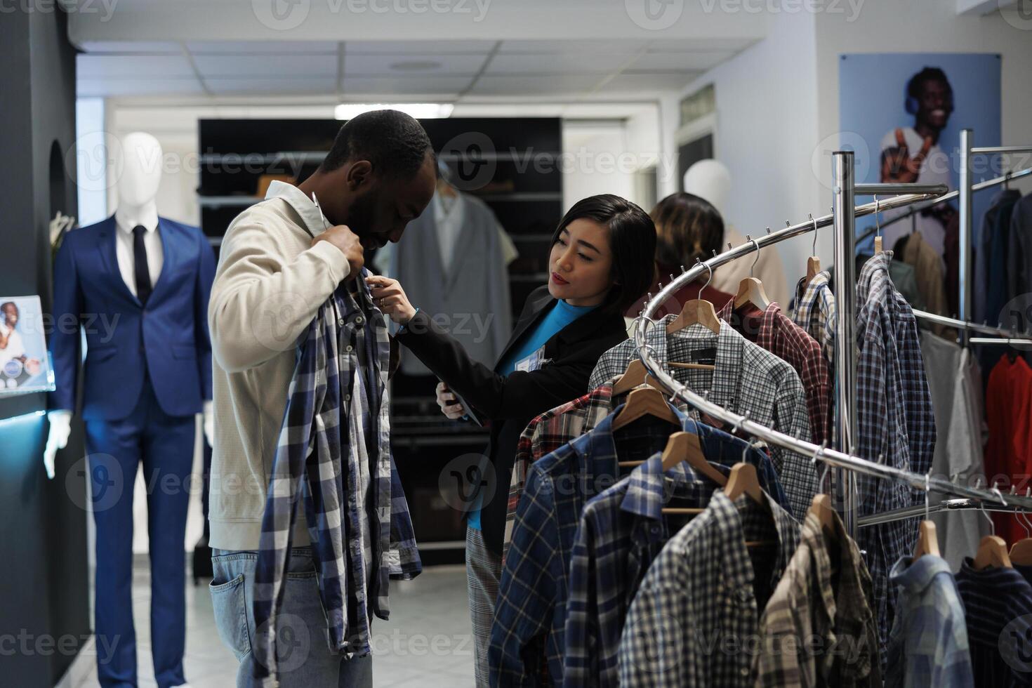 Boutique conslutant providing assistance in choosing casual clothes while customer trying on apparel. Shopping mall showroom worker offering help in selecting casual shirt photo