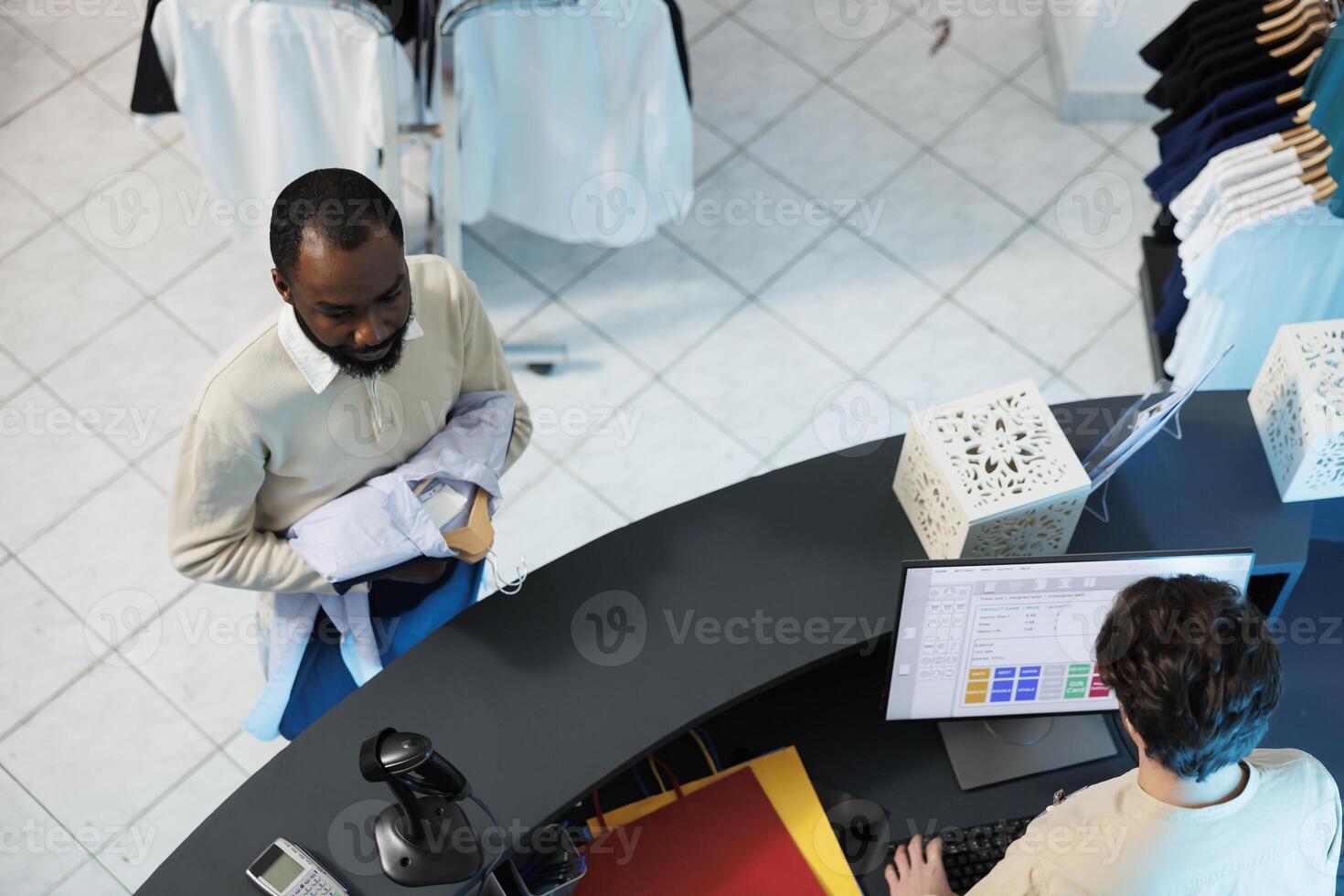 Clothing store worker using cash register software on computer while buyer standing in line at checkout top view. Shopping center employee cashier working at counter desk while customer waiting photo