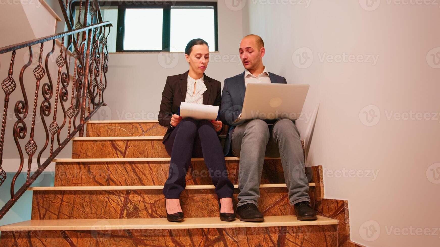 negocio personas mecanografía en ordenador portátil leyendo documentos desde portapapeles analizando informes sentado en escalera en Finanzas corporativo compañía. grupo de profesional gente de negocios caminando en financiero lugar de trabajo. foto