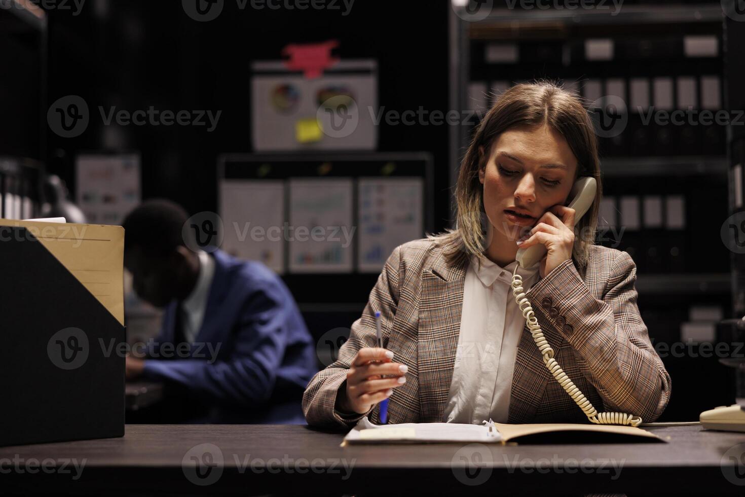 Woman detective working at criminal investigation, discussing crime scene evidence with inspector using landline phone. Police officer analyzing victim report, wanting to bring suspect to justice. photo