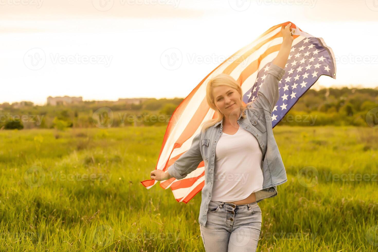 attractive woman holding an American flag in the wind in a field. Summer landscape against the blue sky. Horizontal orientation. photo