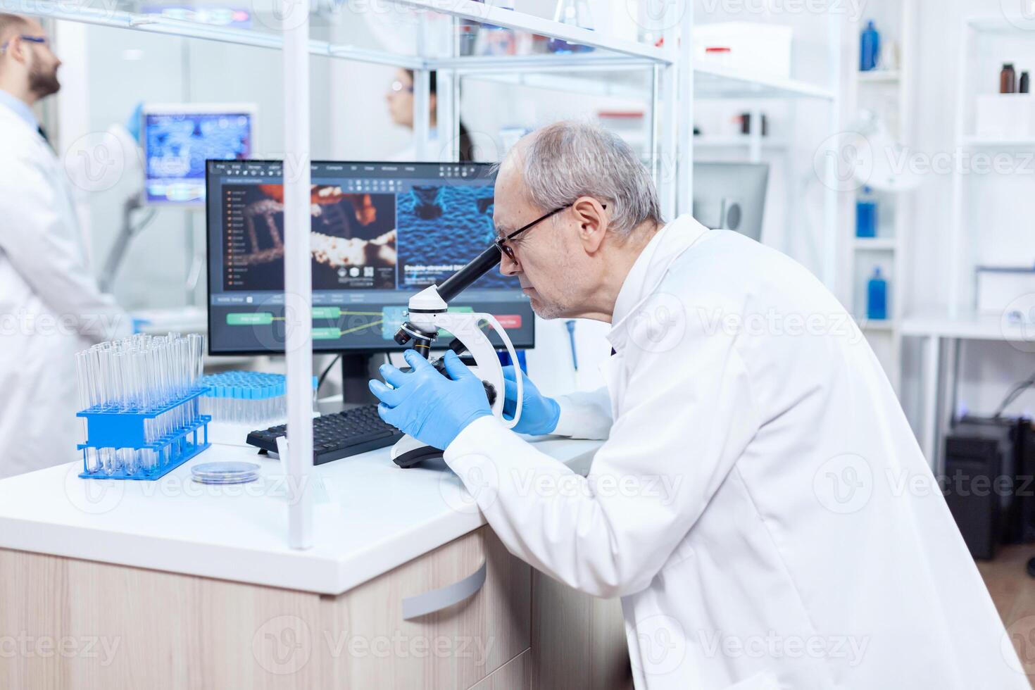 Senior scientist preparing and analyzing microscope slides with busy coworkers. Chemist researcher in sterile lab doing experiments for medical industry using modern technology. photo