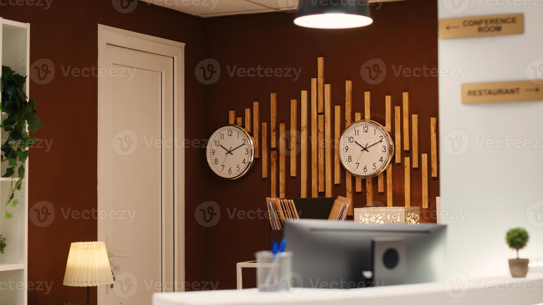 Empty cozy check in front desk in stylish luxurious resort lounge interior filled with plants and clocks on wall. Welcoming hotel reception counter ready for arriving guests photo