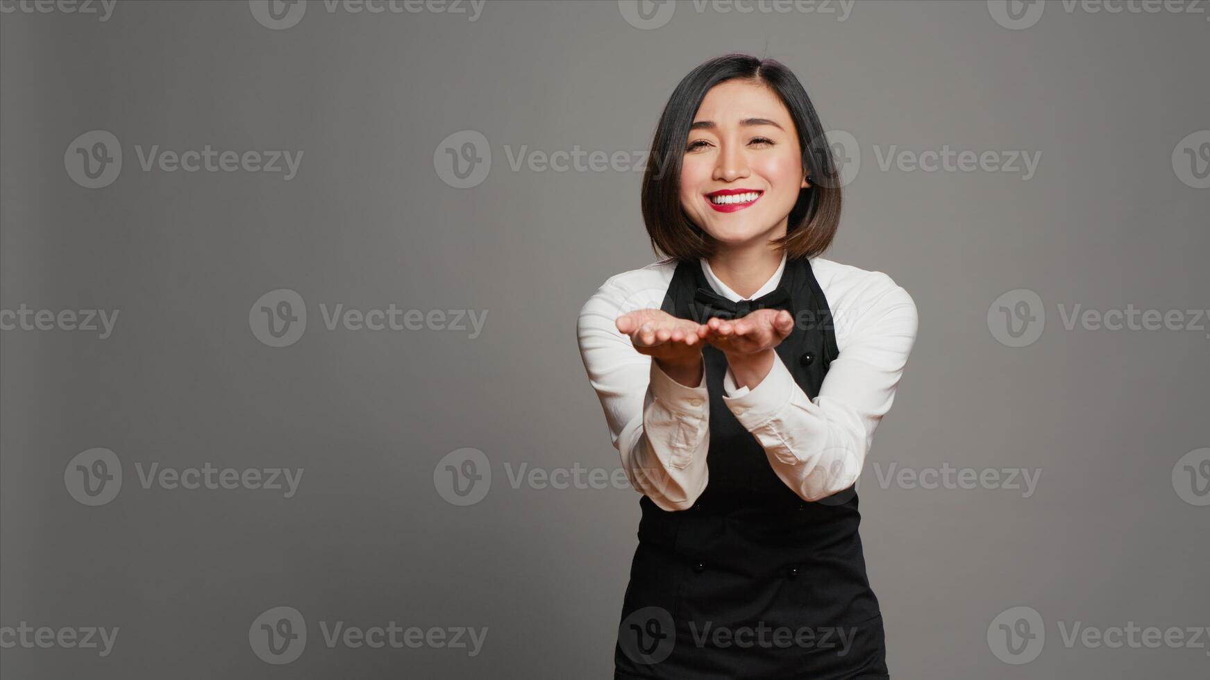 Cute flirty waitress blowing air kisses in front of camera, acting romantic with sweet gesture. Asian restaurant employee posing with a kissy facial expression, catering industry. Camera A. photo