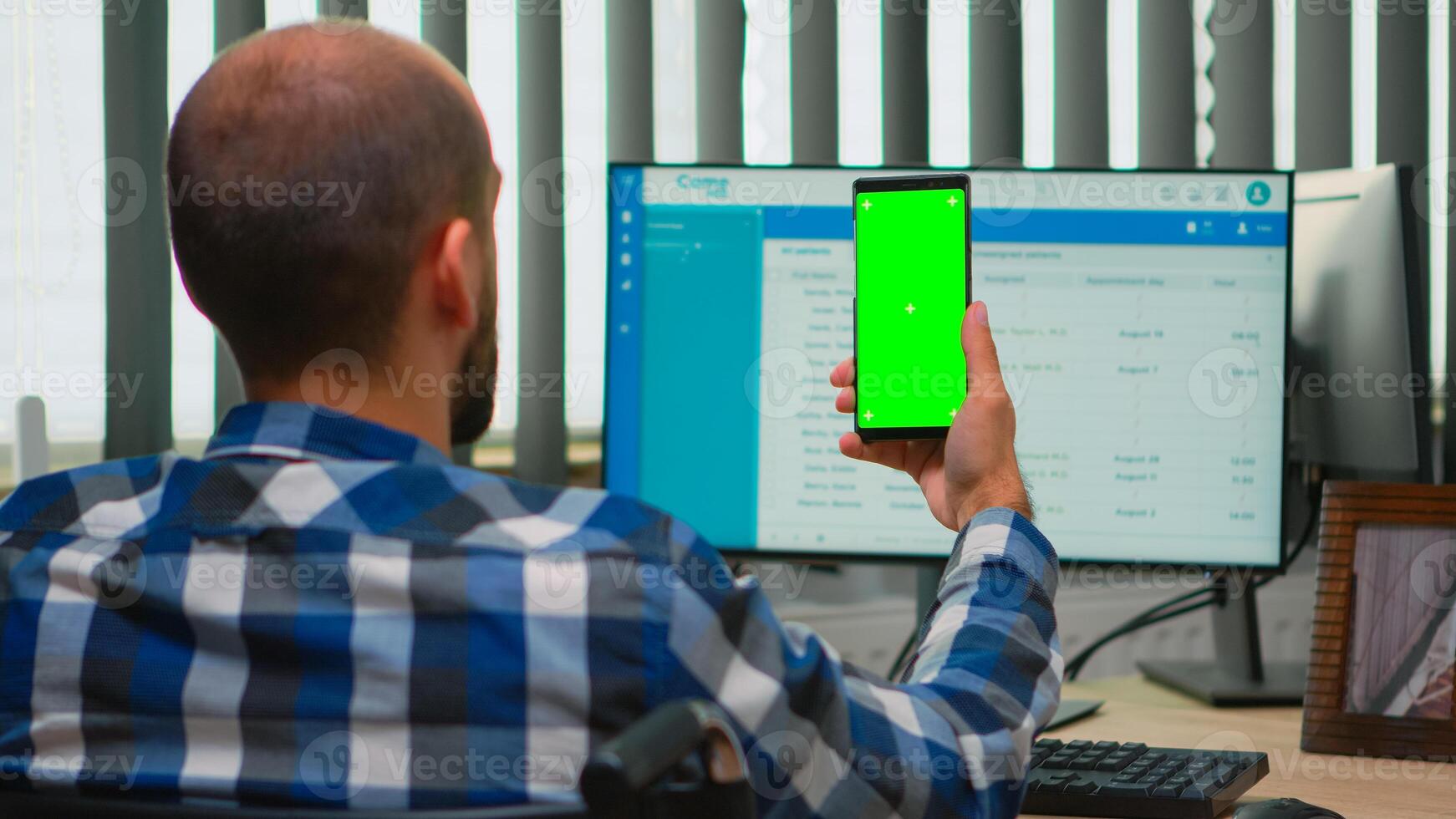 Immobilized businessman in wheelchair using smartphone with greenscreen for videomeeting. Handicapped disabled freelancer looking at display with chroma key, mockup talking with remotely colleagues photo