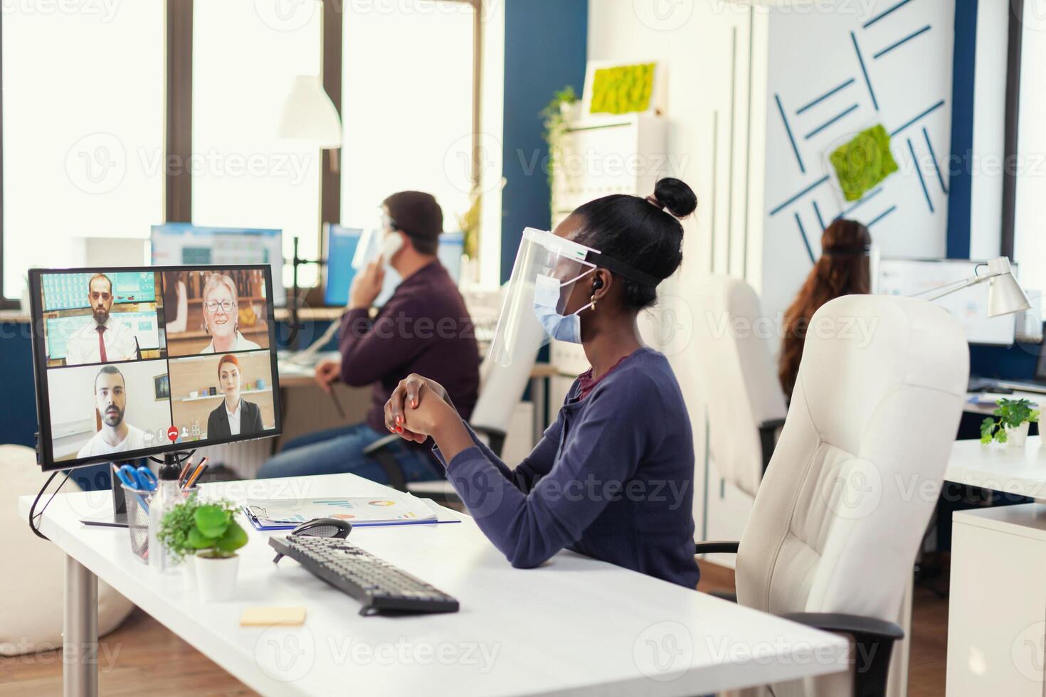 African entrepreneur having a video conference during covid19 wearing face mask. New normal business office Multiethnic team working respecting social distance during global pandemic with coronavirus. photo