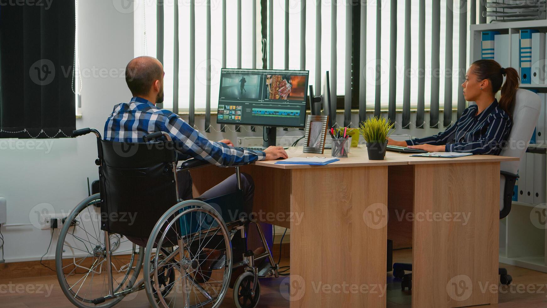 equipo de videógrafos trabajando a vídeo proyecto creando contenido, hombre blogger sentado en silla de ruedas en moderno empresa oficina. discapacitado persona de libre dedicación edición imágenes post-producción en estudio. foto