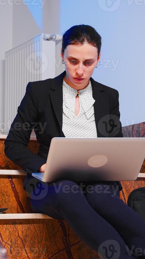 Focused business employee working on to finish a corporate job deadline at late hours sitting on staircase of business building. Serious tired entrepreneur doing overtime at financial project. photo