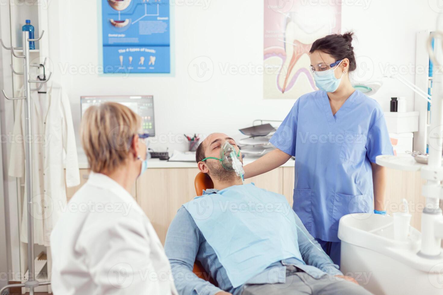 ortodoncista asistente poniendo oxigeno máscara a paciente analizando dientes dolor durante estomatología cita. médico equipo trabajando en odontología clínica oficina comprobación diente preparando para cirugía foto