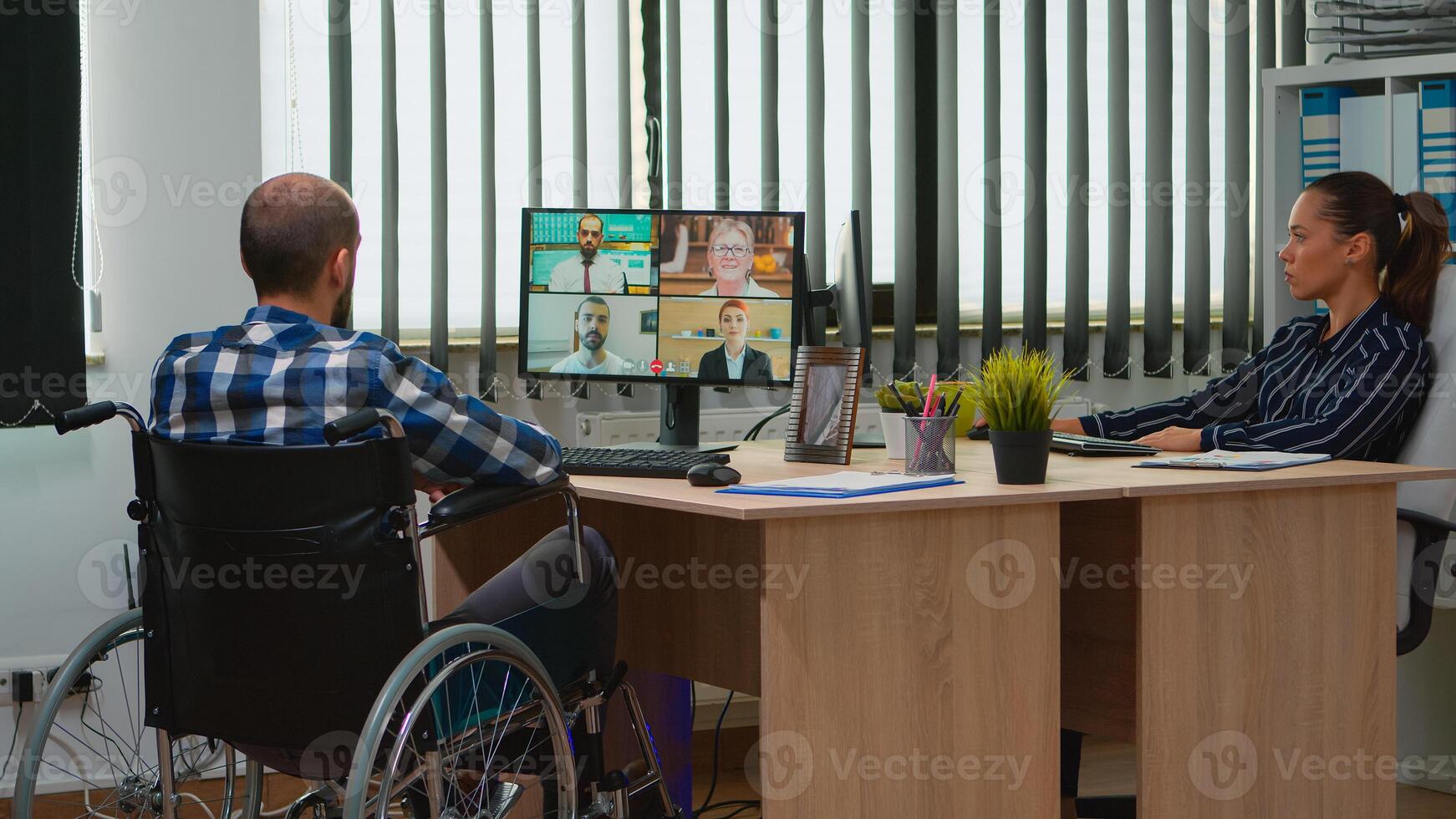Paralysed, immobilized freelancer in wheelchair having videomeeting discussing online with coworkes in business office. Handicapped businessman working in financial company using modern technology. photo
