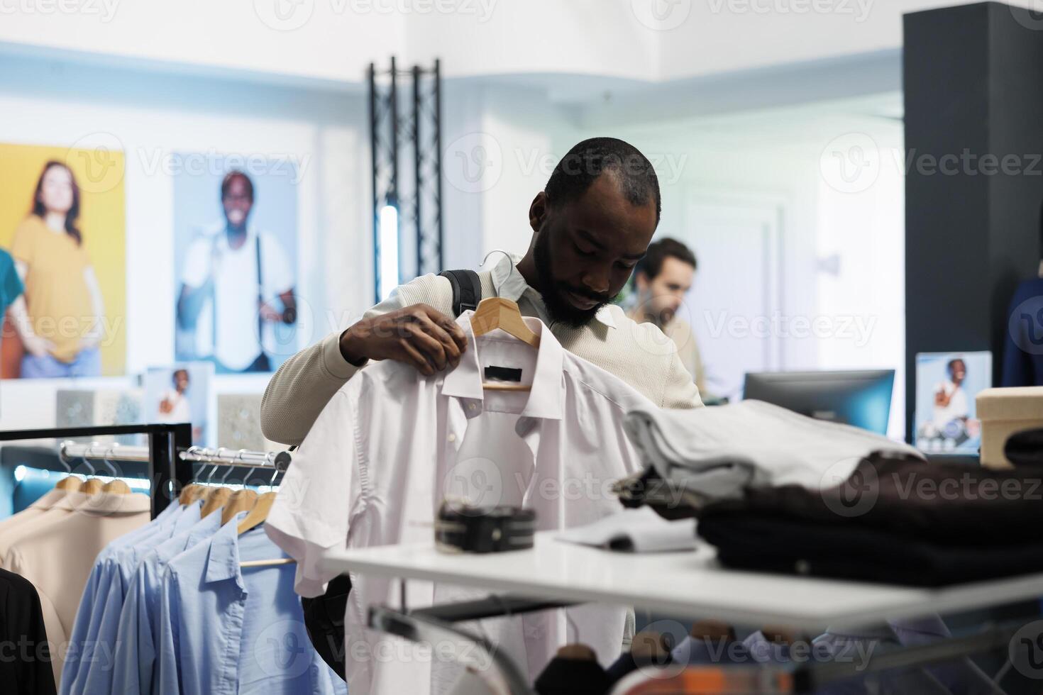 ropa Tienda cliente participación formal camisa a cuerpo, considerando Talla y ajuste antes de haciendo compra. africano americano hombre molesto en atuendo mientras elegir prenda en boutique foto