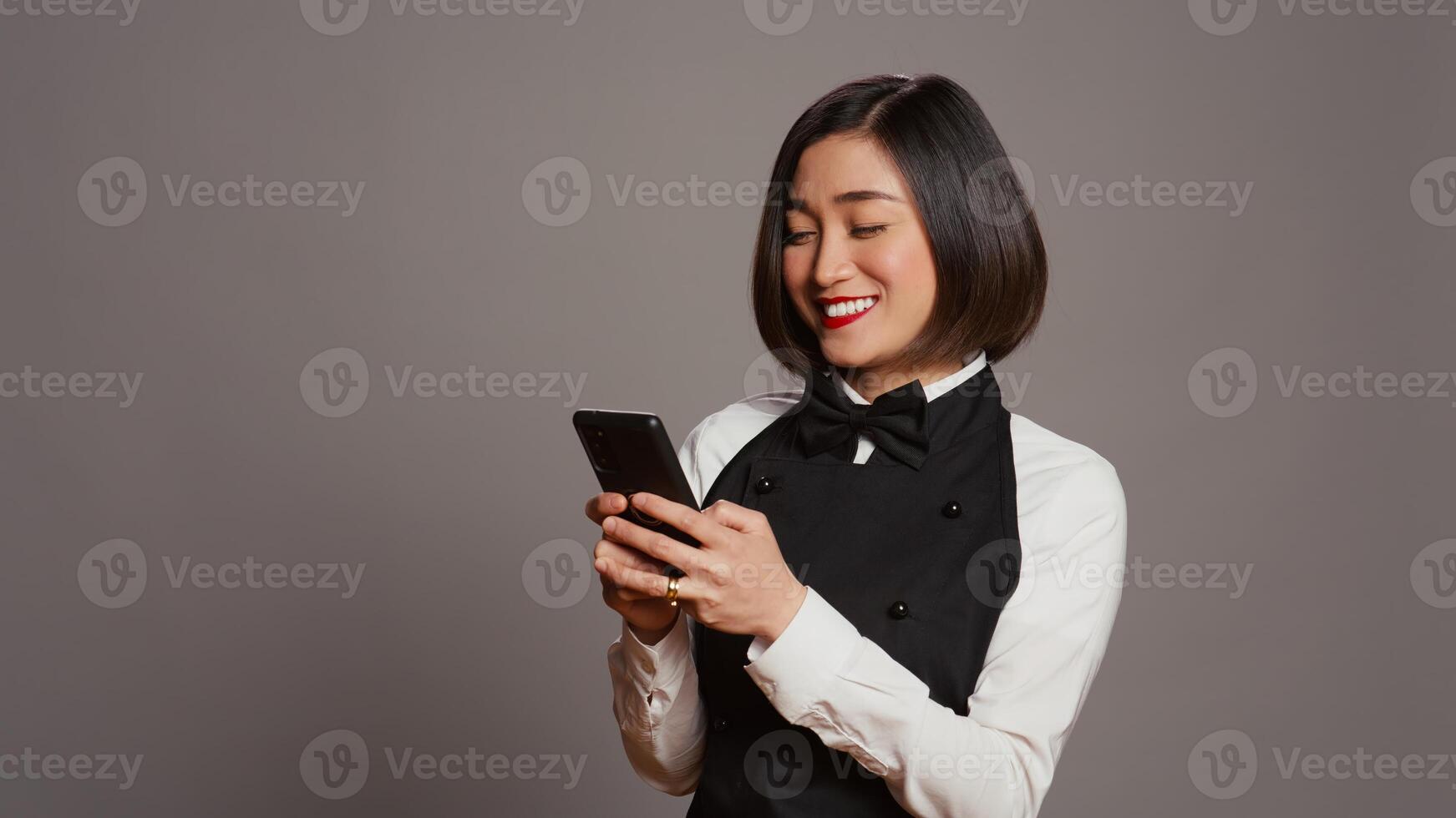 Restaurant hostess texting messages to confirm reservations on phone app, working in catering and serving industry. Asian waitress using smartphone online websites, social media. Camera B. photo