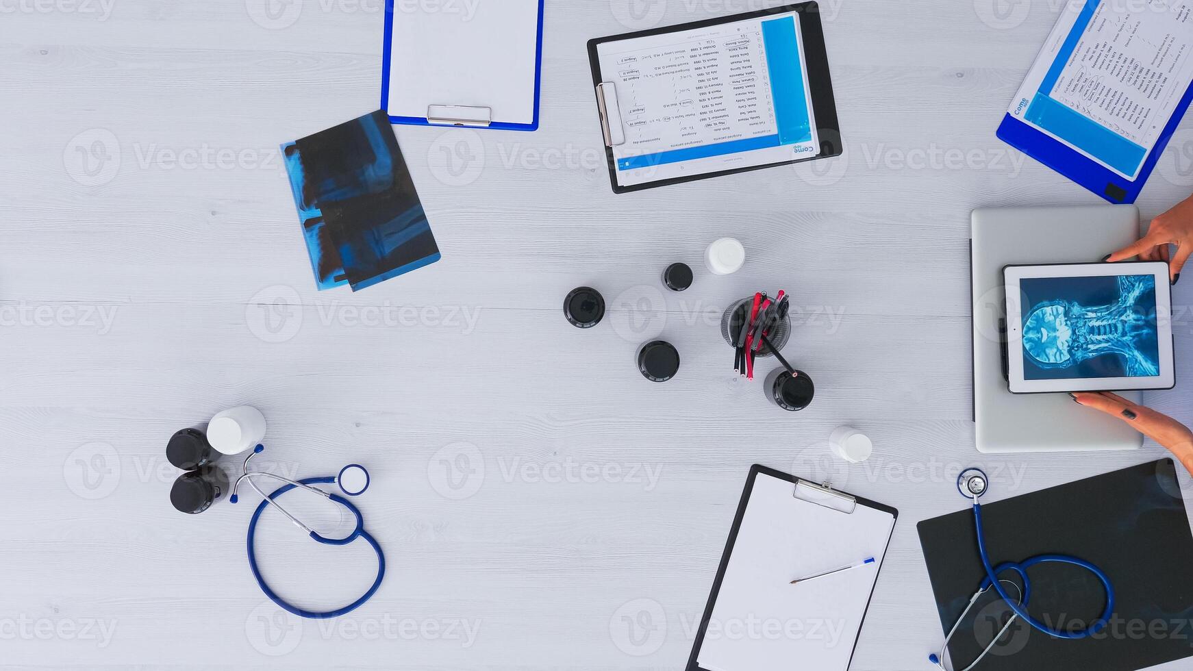 Top view of doctor closing laptop and analysing digital x-ray using tablet, working in medical office sitting on desk with stethoscope and digital devices. Studying on clinic on copy space, flat lay photo