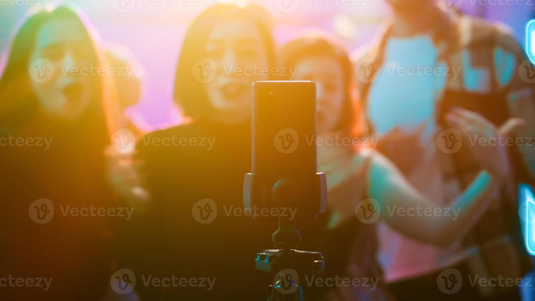 Influencer filming vlog at club party, using smartphone to record video of her and her friends having fun on dance floor. Happy woman enjoying night out clubbing with people, social media. photo