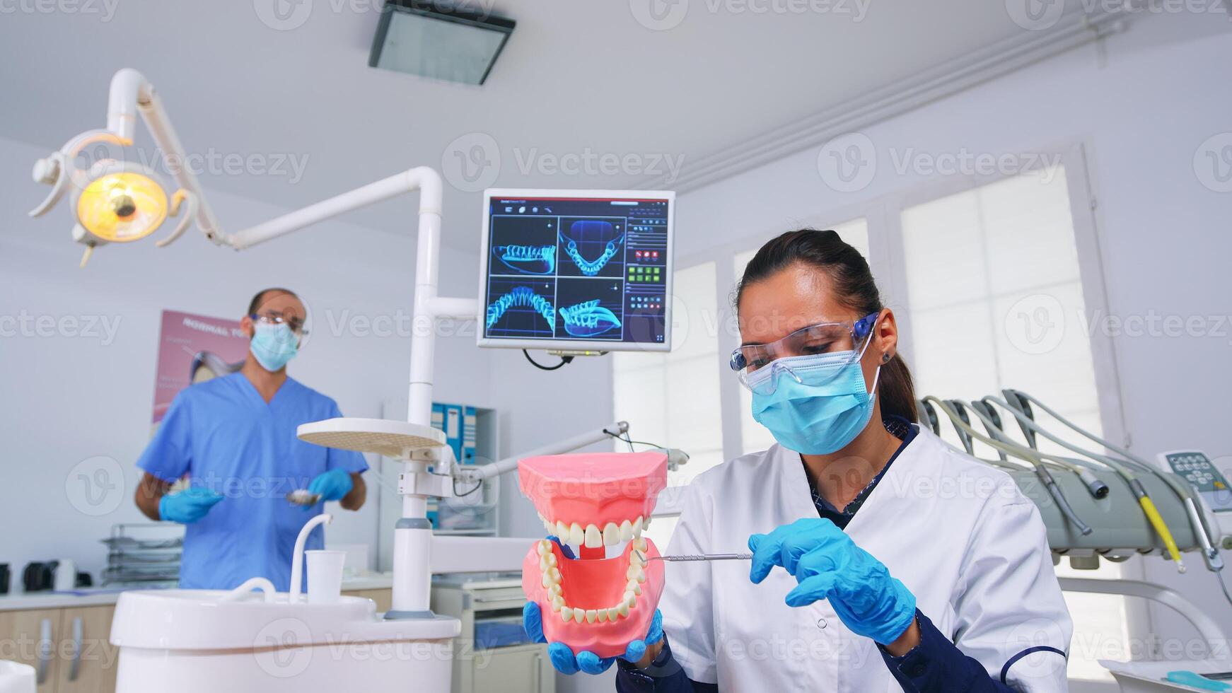 paciente pov de dentista demostración correcto camino de limpieza dientes vistiendo en dental oficina utilizando dientes médico esqueleto accesorio. estomatólogo vistiendo proteccion máscara durante cuidado del calor cheque foto