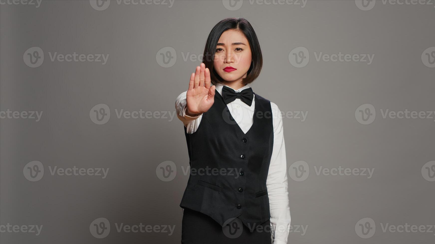 Asian administrator showing stop sign with palm raised in studio, presenting negative symbol and expressing disapproval. Woman receptionist doing no gesture, being displeased. Camera A. photo