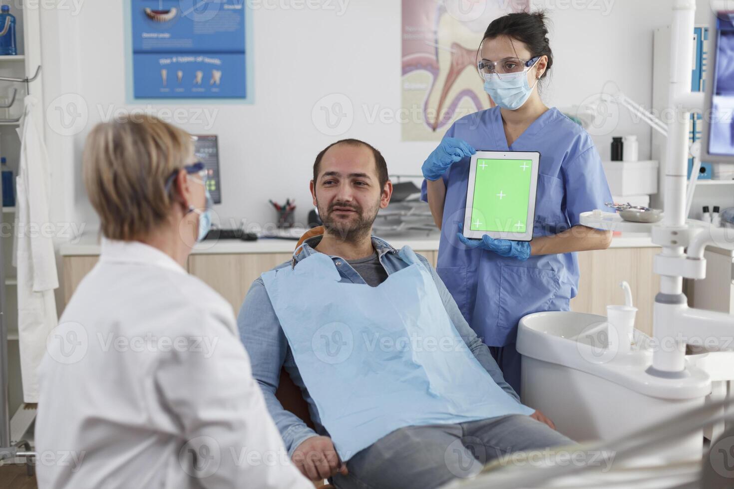 Stomatology medical team discussing dentistry treatment with patient during stomatological consultation in dental office. Nurse holding mock up green screen chroma key tablet with isolated display photo