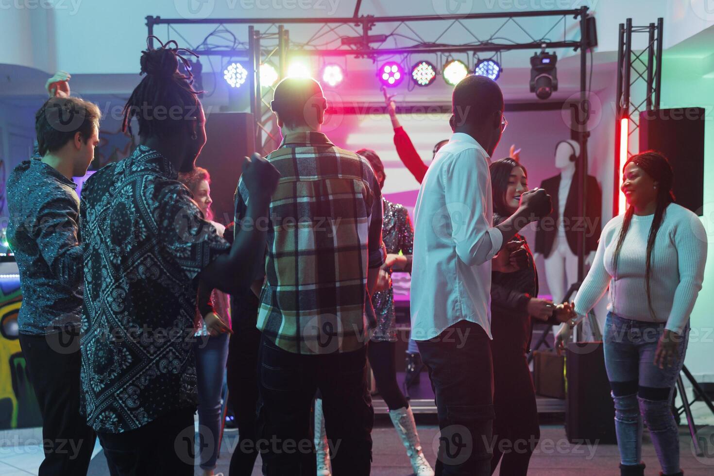 Young people enjoying concert on dancefloor with spotlights during live music performance in nightclub. People crowd clubbing and dancing while attending party at nighttime photo