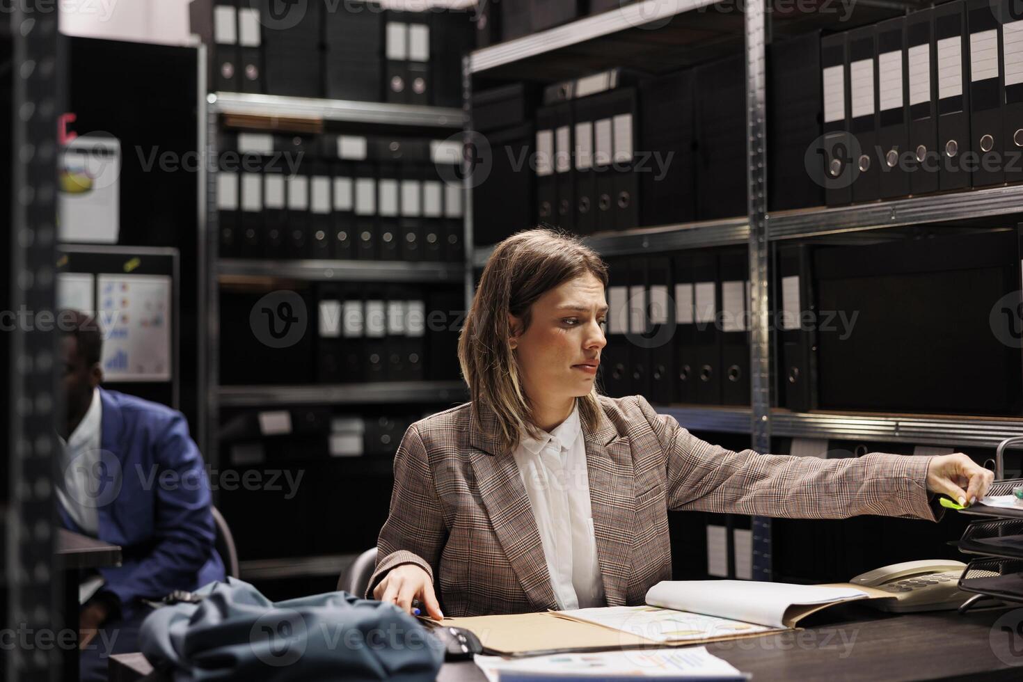 Investigator analyzing police report, checking crime case confidential information. Private detective in formal suit discovering mysterious victim files, working overtime in arhive room photo