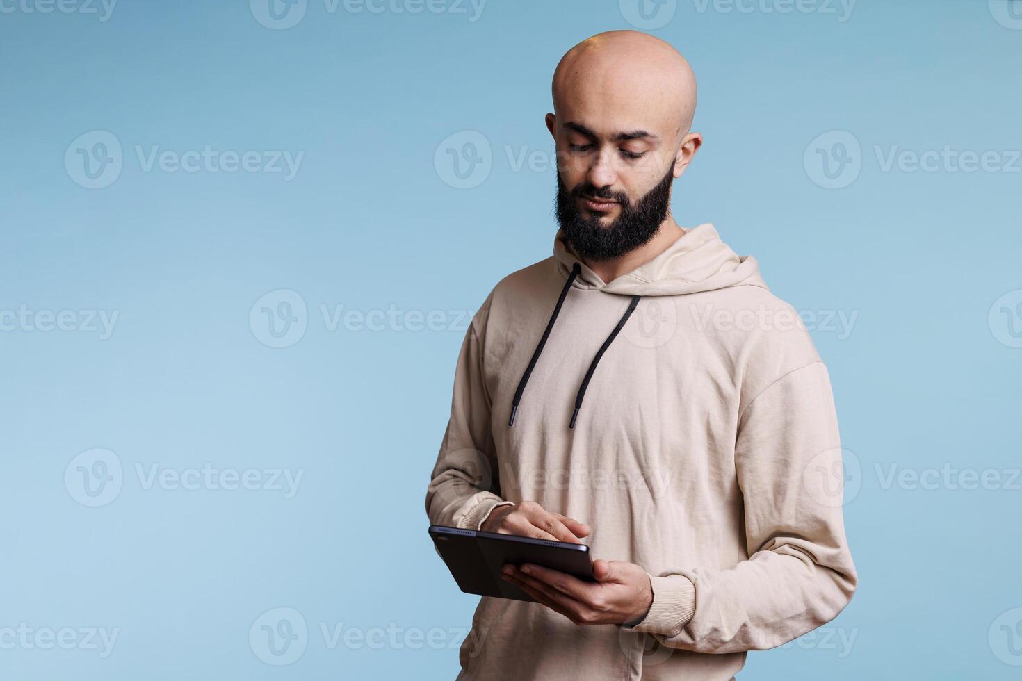 Arab man using digital tablet application, browsing internet and writing online message. Young person texting in social media and while tapping on portable gadget touchscreen photo
