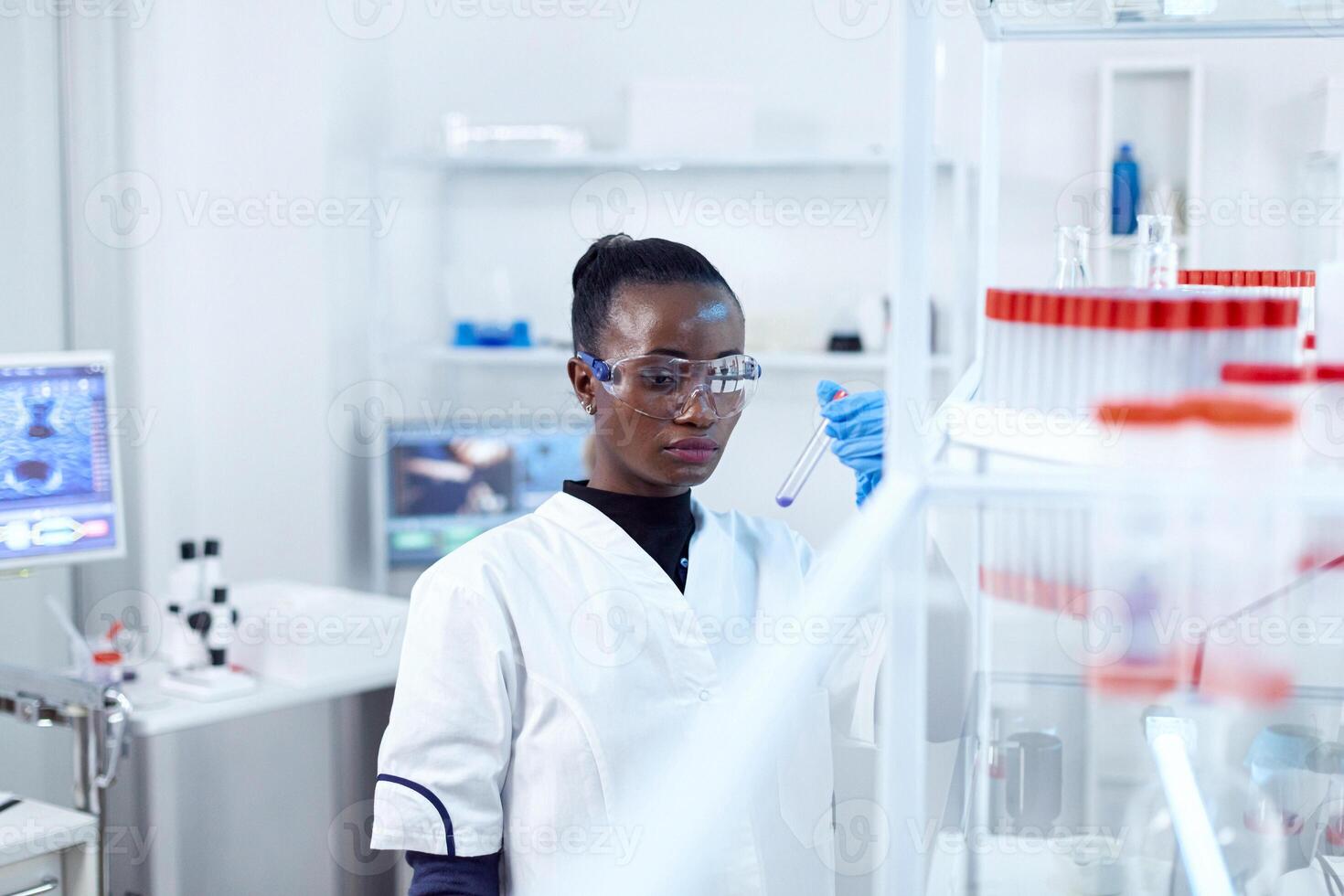 africano científico participación prueba tubo con azul líquido para médico objetivo. negro investigador en estéril laboratorio conductible farmacología experimentar vistiendo abrigo. foto