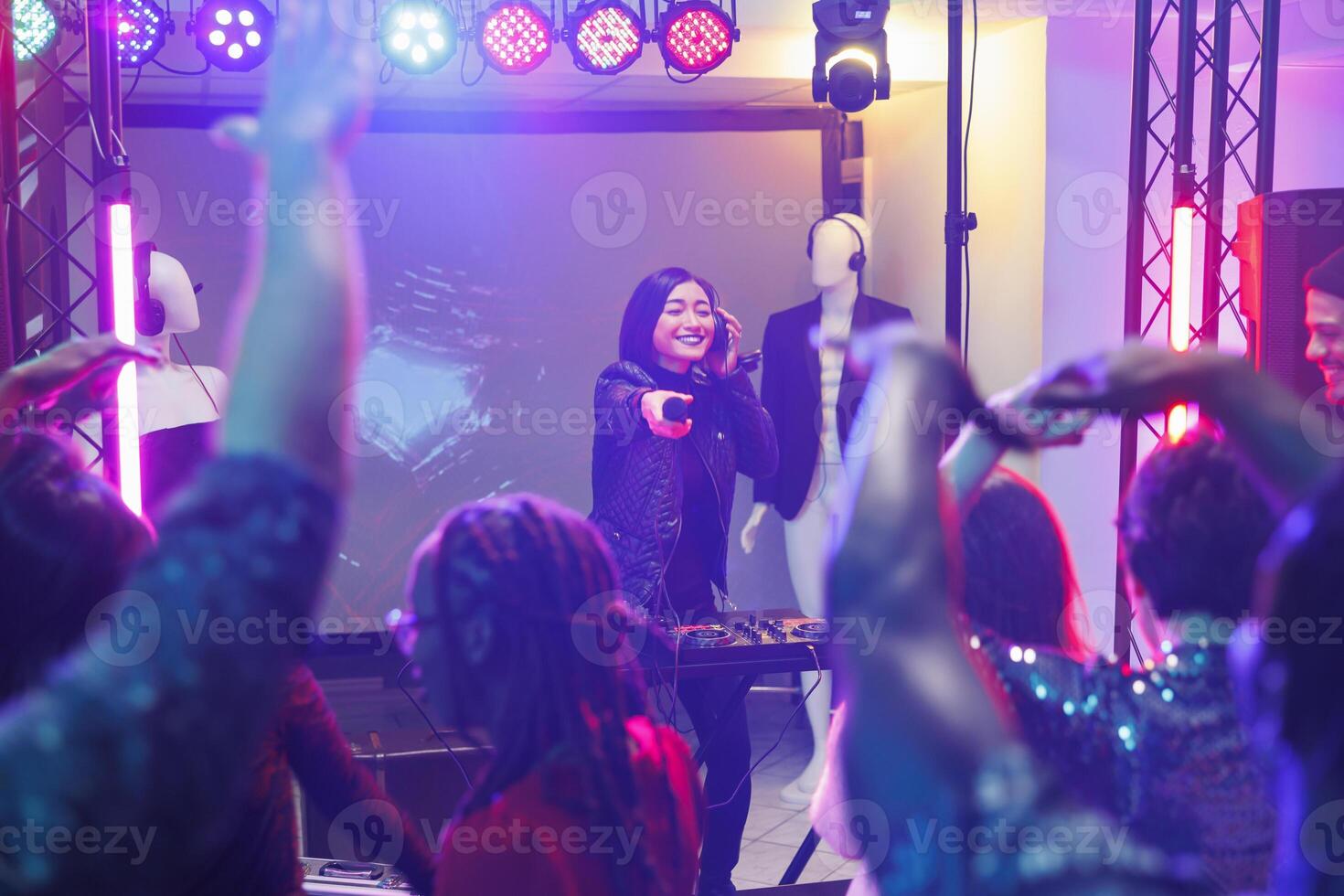 Woman dj offering audience to sing in microphone during performance on stage. Crowd clubbing and partying while enjoying nightlife at electronic music concert on nightclub photo