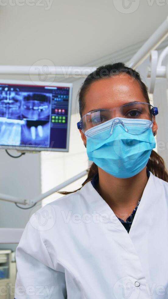 paciente pov en dental silla haciendo ejecutando periódico dientes cheque en moderno estomatológico clínica. odontología médico Encendiendo el lámpara y examinando persona vistiendo proteccion máscara y lentes. foto