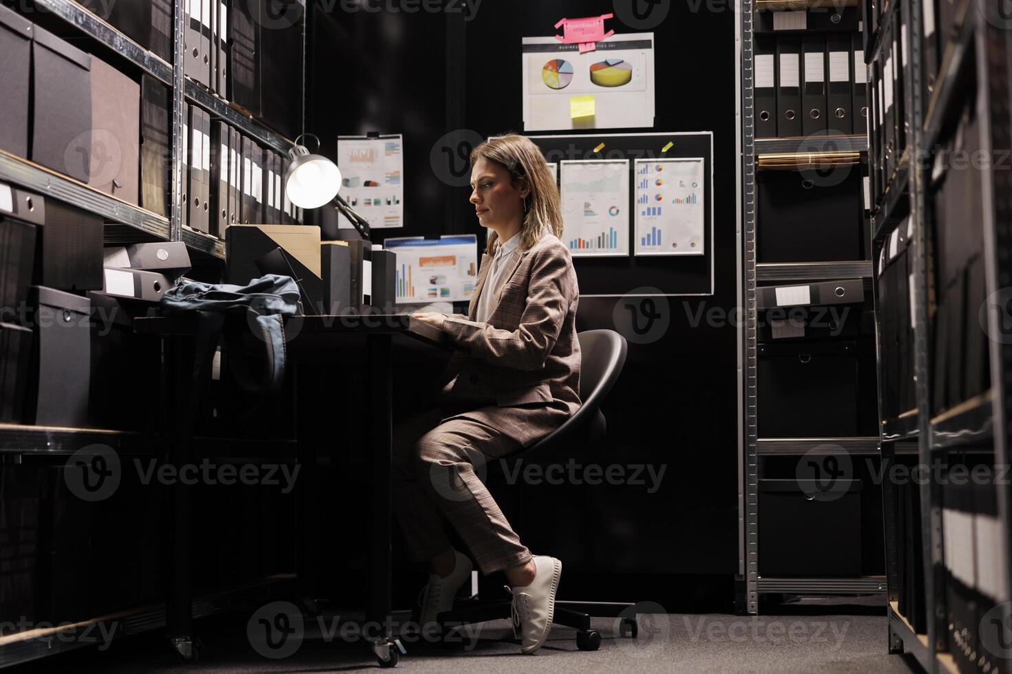 Businesswoman reading bureaucracy report, organizing corporate papers in storage room. Caucasian bookkeeper checking administrative documents, working overtime at office depository photo