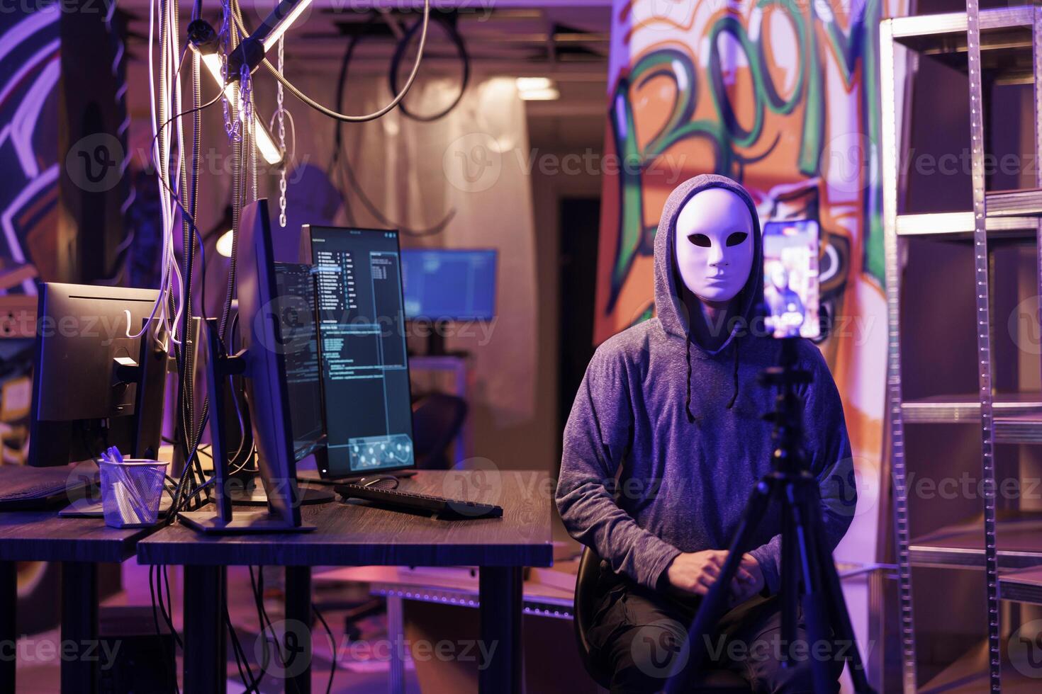 Anonymous hacker recording threat video with ransom message on smartphone to steal privacy information. Internet criminal calling victim using mobile phone in abandoned warehouse photo