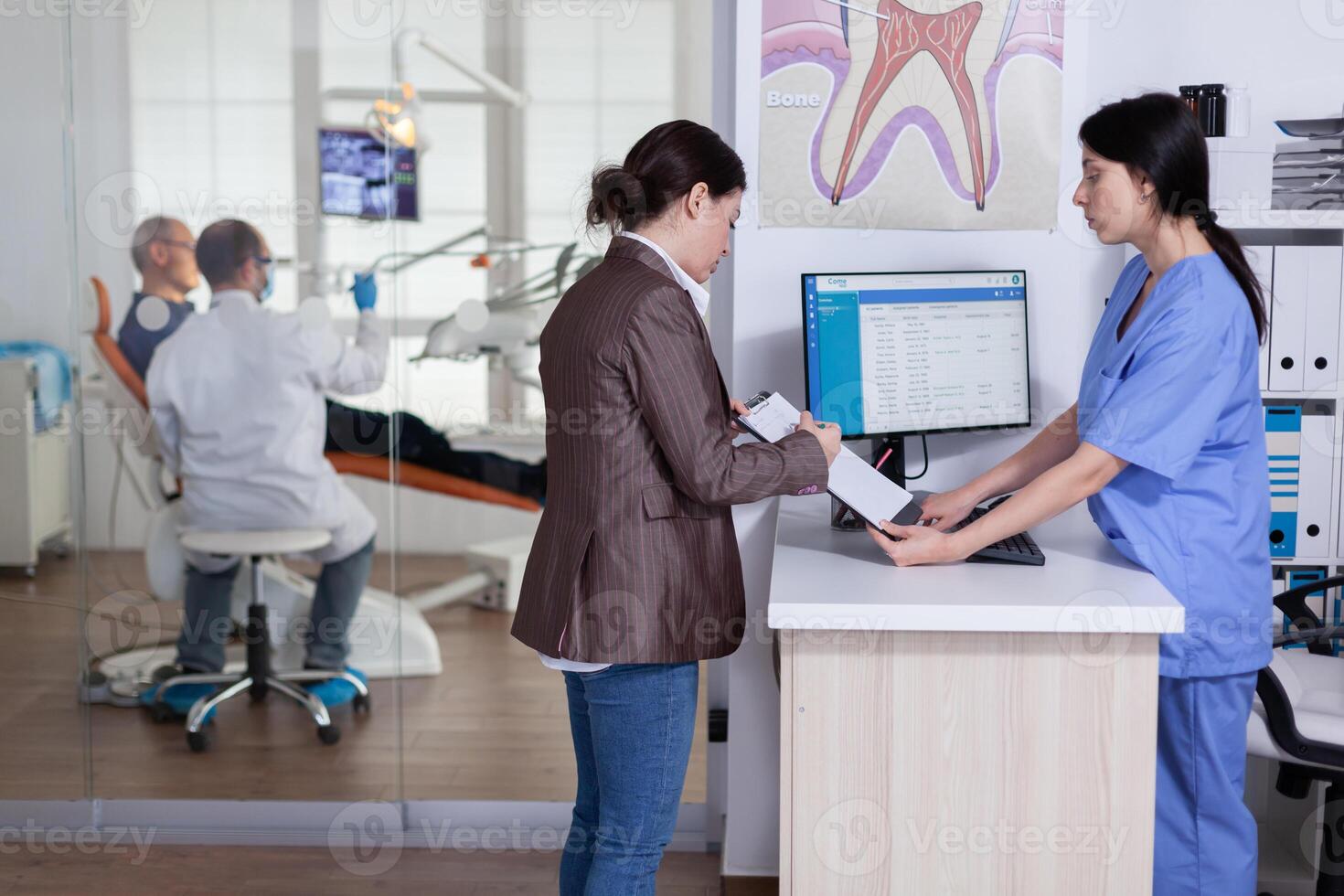Young lady asking informations filling in stomatological form while patients talking sitting on chair in waiting area. People speaking in crowded professional orthodontist reception office. photo