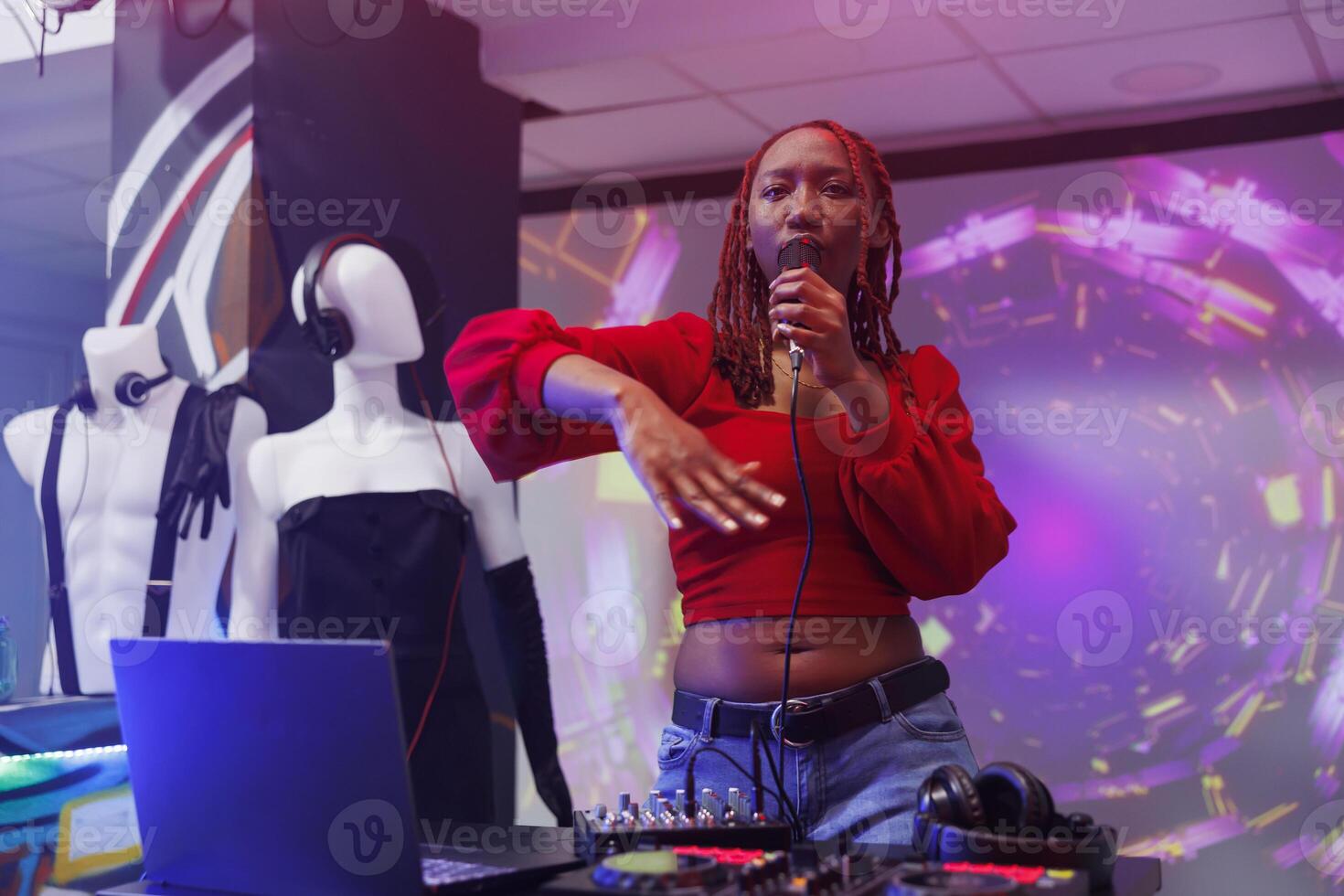 African american singer performing on stage at nightclub party. Woman dj singing in microphone and mixing tracks with electronic music digital station at club discotheque photo