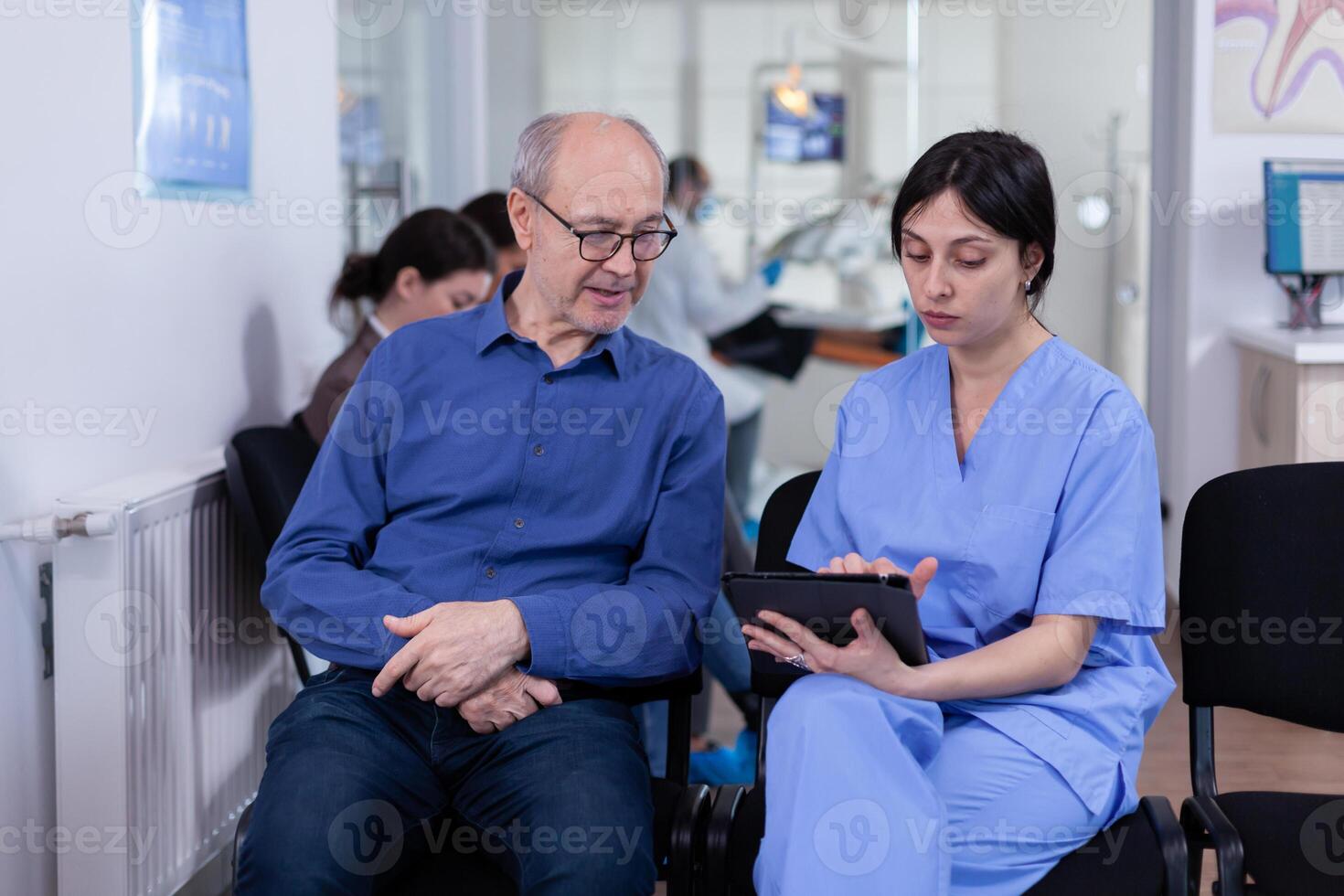 enfermero tomando notas en tableta ordenador personal que se discute con mayor paciente en dental oficina, explicando diagnóstico. asistente relleno escritura cuidado de la salud forma. odontología hospital. foto