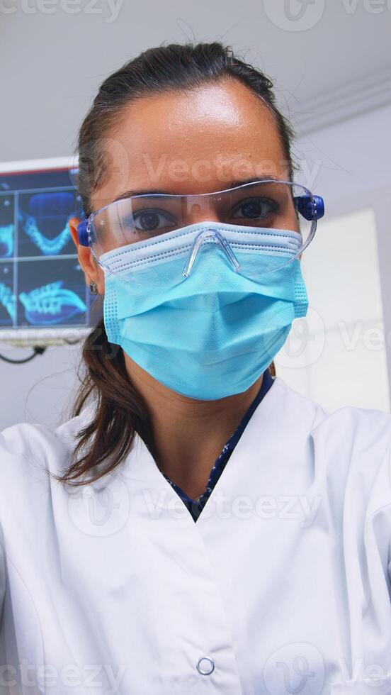 Patient pov to stomatologist performing examination and taking care of teeth using dental tools in modern clinic. Doctor and nurse working in modern orthodontic office wearing protection mask photo