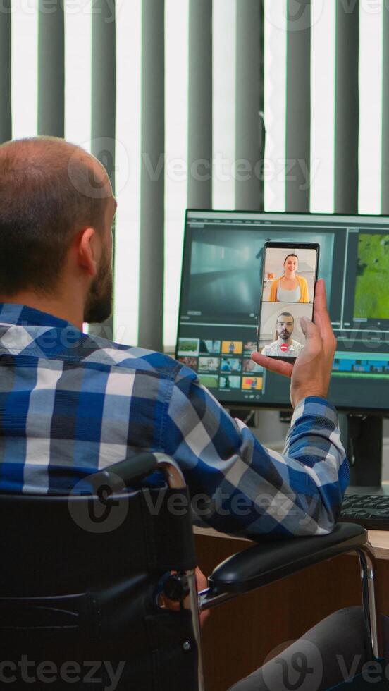 Handicapped videographer in wheelchair talking on webcam with cowerkers while editing a video project creating content in modern company office. Creator blogger working from photo studio.