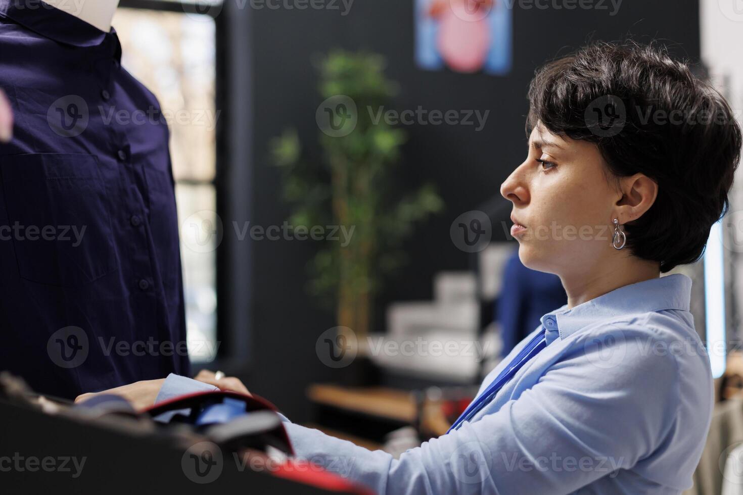 Store worker arranging trendy accessories and clothes, preparing fashion store for opening. Employee working with fashionable merchandise, checking new collection price in modern boutique photo