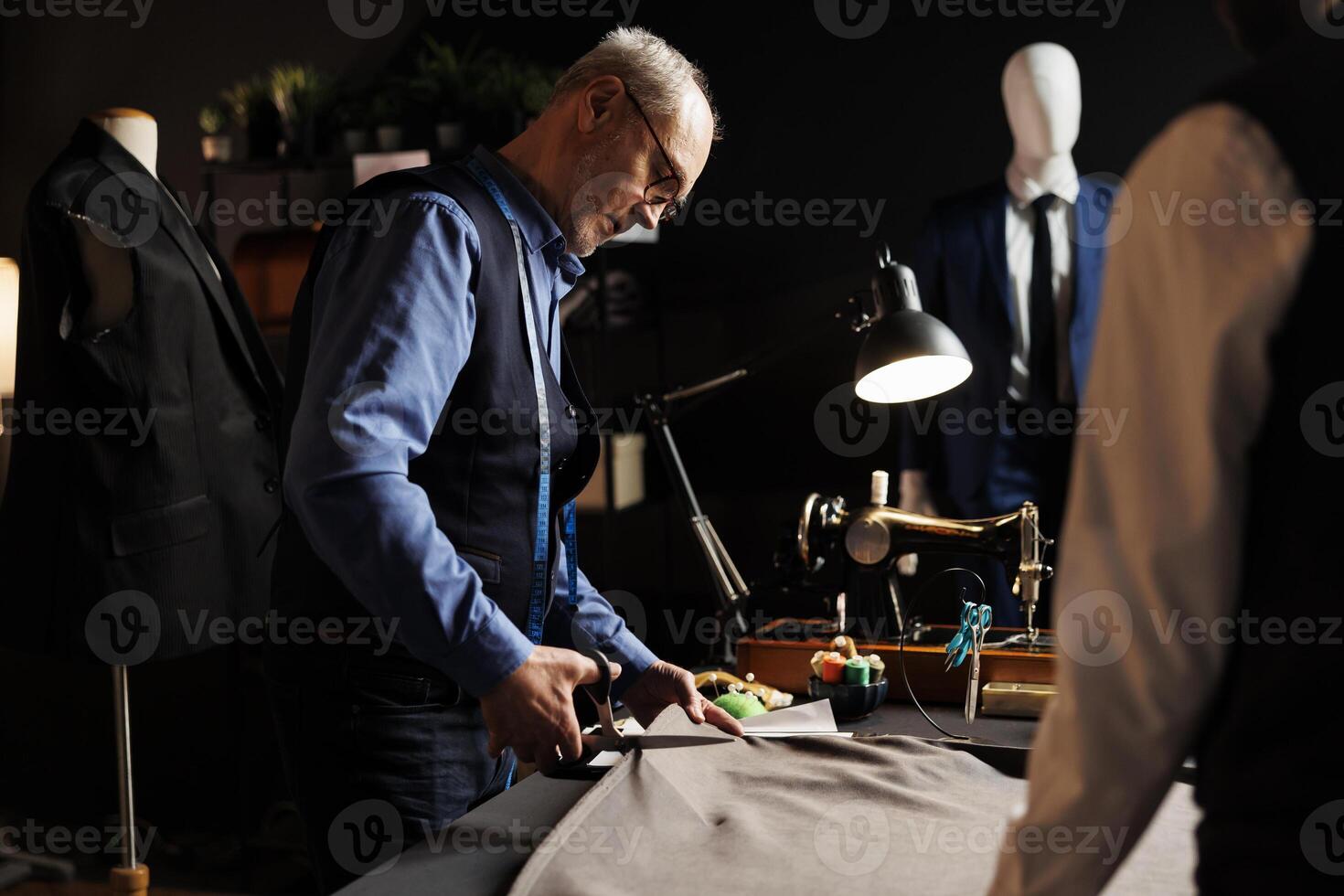 preciso experimentado mayor sastre fabricación traje en sastrería estudio espacio de trabajo, corte tela material con tijeras. proceso de fabricación próximo hecho a la medida Moda diseño colección foto